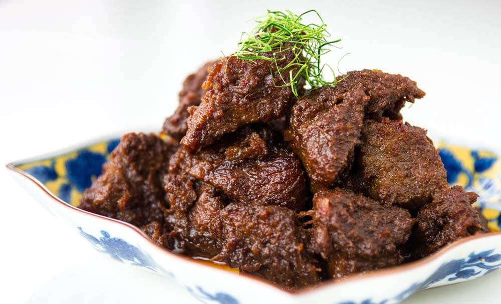 Potret mendetail rendang ayam dengan saus kental dan warna merah kecokelatan