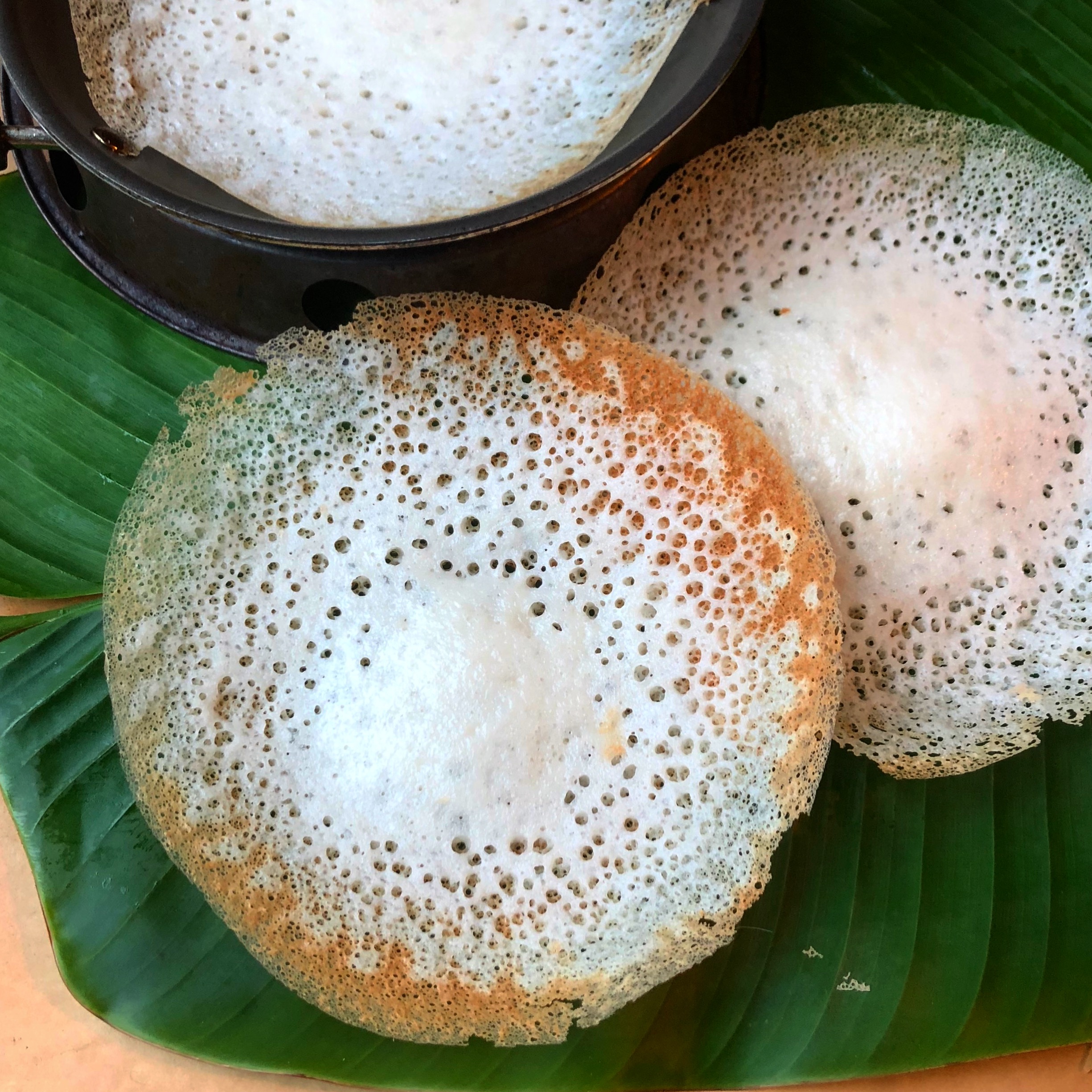 Appam being cooked in a non-stick pan, showing its characteristic shape.