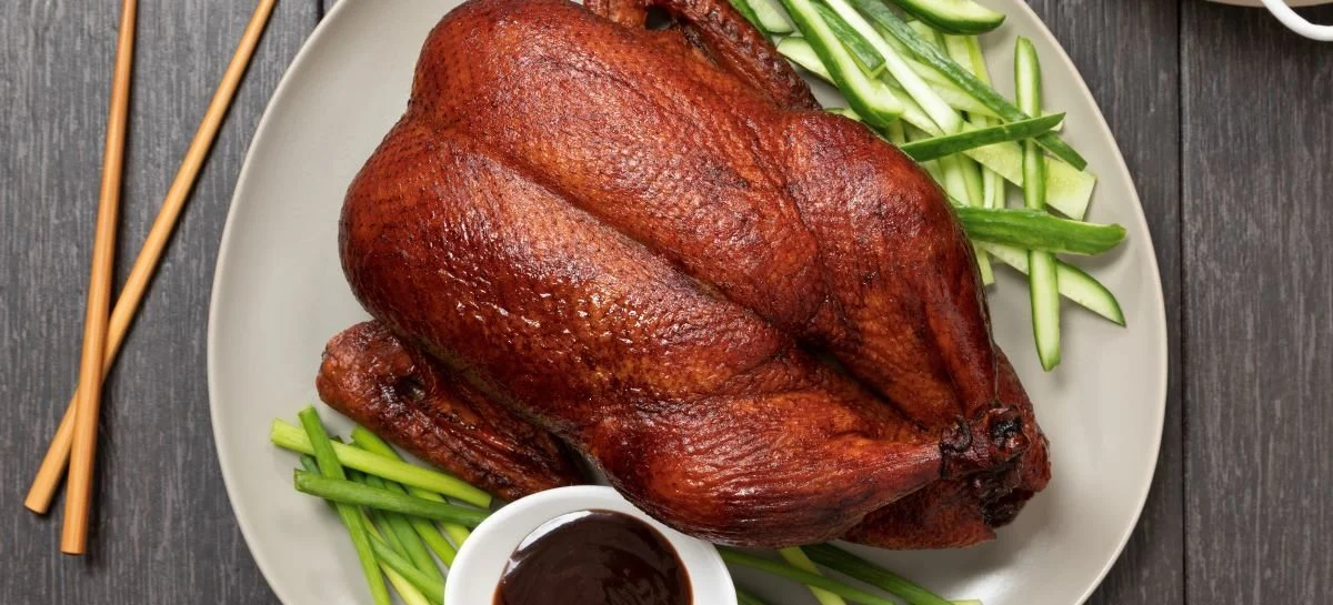 An elegantly presented plate of Peking Duck with hoisin sauce, cucumber, and spring onions