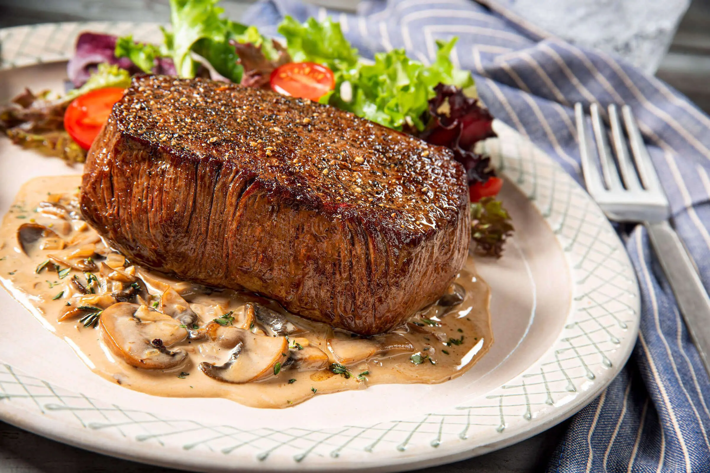 A juicy ribeye steak served on a wooden board with rosemary and garlic. 